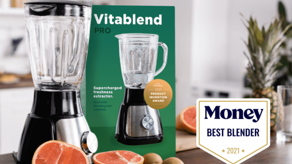 A high-end blender sits on a kitchen counter alongside the box it came in. The Money Best Blender award logo is clearly visible on the advertisement.